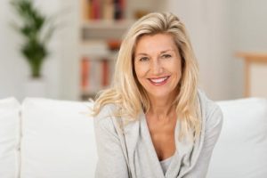 Lovely middle-aged blond woman with a beaming smile sitting on a sofa