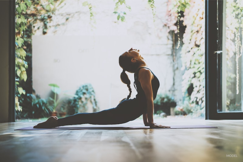 Woman practicing yoga in her house. Performing an up-dog posture.