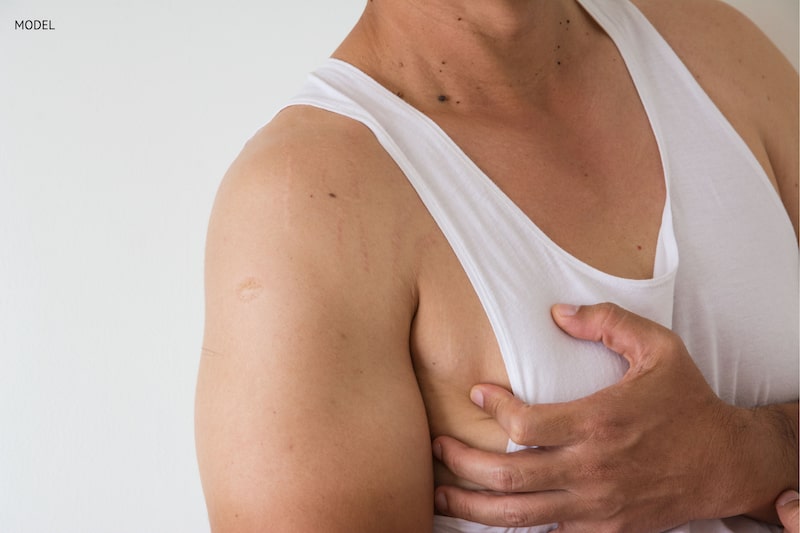 Man cupping his hand over his breast wearing a white t-shirt.