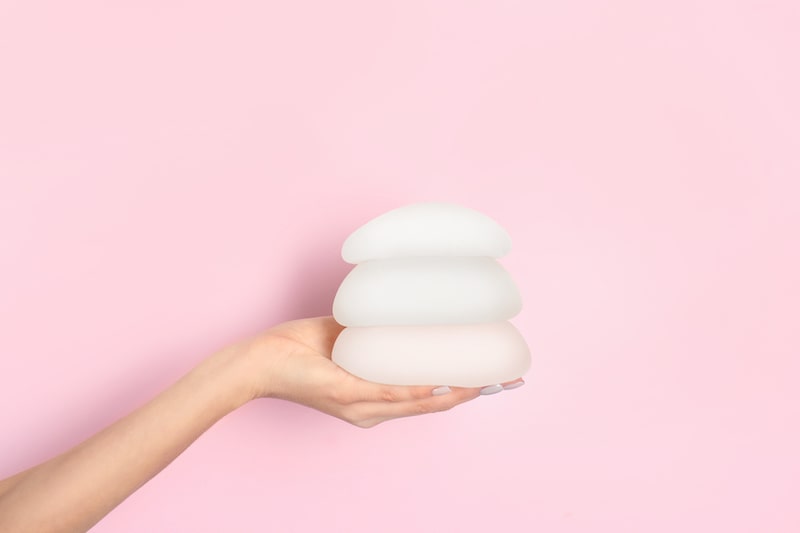 A woman holding three breast implants of different sizes.