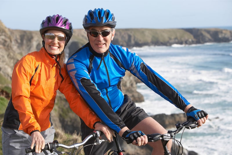 Middle age couple bike riding with the ocean in the background
