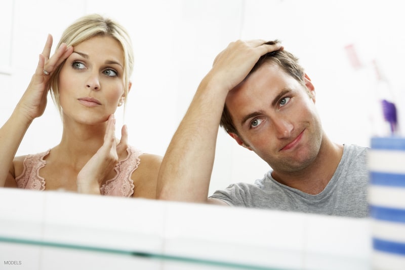 Attractive woman and man looking at their reflections in the mirror, frustrated with signs of aging