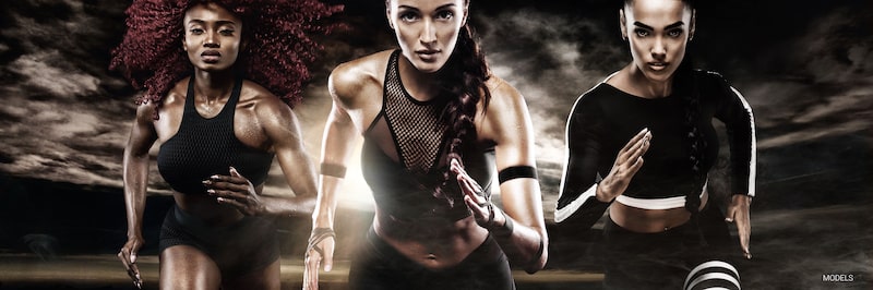 Three athletic women sprinters face the camera while racing.