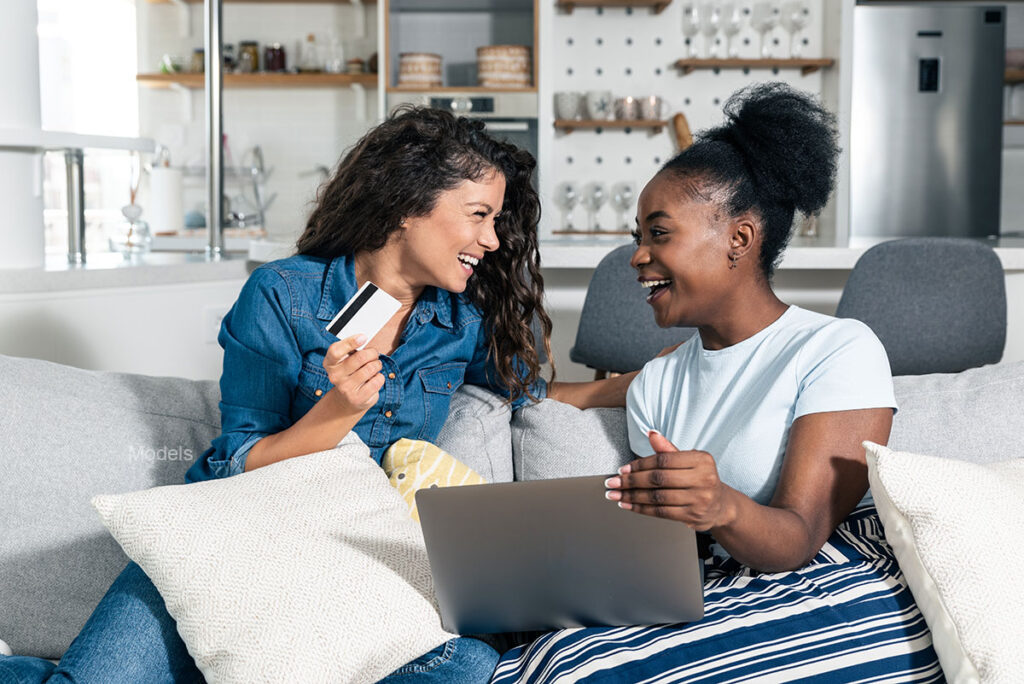 two friends smiling and sitting together and one is holding a payment card