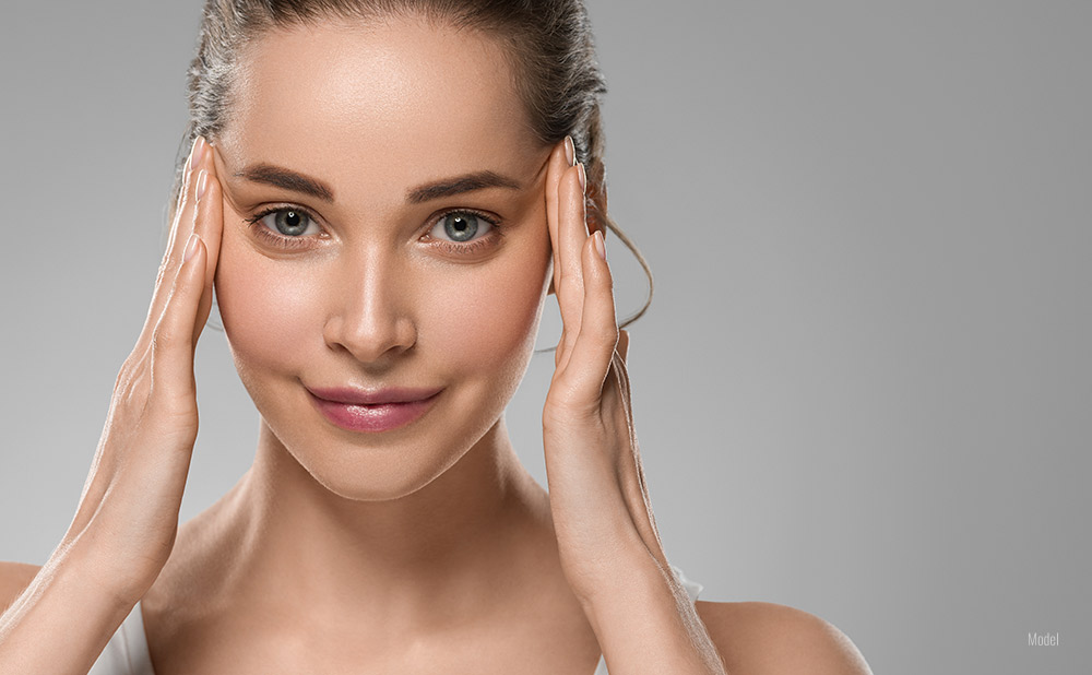 Young woman with her hands at her temples smoothing out wrinkles